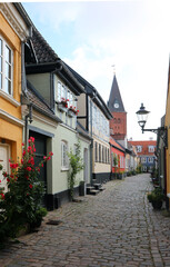 cobblestone alley with northern Danish houses featuring grid windows flower beds and a bell tower