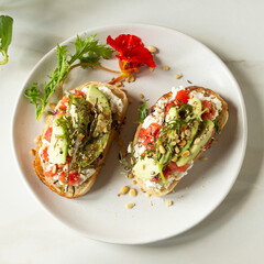 plate of bruschetta with avocado, ricotta and tomatoes on a light table