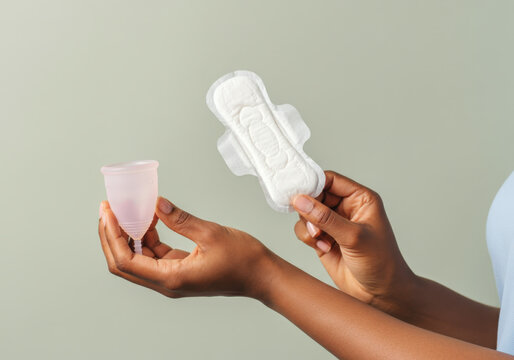 Woman comparing a reusable menstrual cup and a disposable sanitary pad for her period hygiene