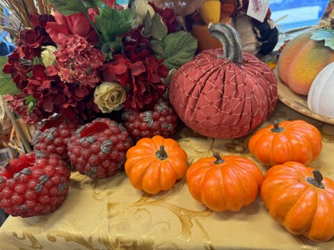 an autumn-themed arrangement featuring small orange pumpkins, red textured candles, and a floral centerpiece