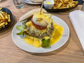 Delicious artisanal hamburger topped with a poached egg and creamy sauce, served with crispy fries in a cozy burger restaurant setting.