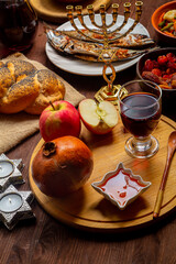 Challah, honey, apple and pomegranate and wine and chelnt and fish on the table with menorah and burning candles in honor of Rosh Hashanah