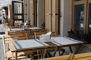 Outdoor empty coffee and restaurant terrace with wooden tables, vintage chairs and linen napkins in Europe. Cafe terrace on the pedestrian street. A set table is waiting for customers.