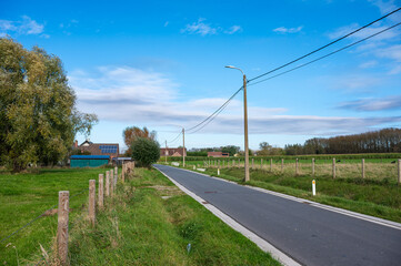 Fototapeta premium Road throguh farmland passing by farmhouses at the Flemish countryside around Zottegem, East Flanders, Belgium