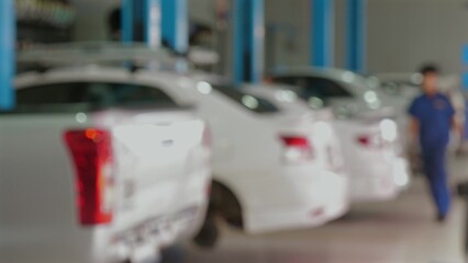 Blurred view of busy automobile repair shop with multiple white cars parked in garage, mechanic walking in background. Automotive Maintenance and Repair.