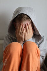 A sad, broken boy covering his face with his hands