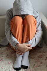 Broken boy sitting curled up on bed, bright colors © Gosia