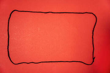 The red background is framed with a black rope. The line is long and thin, and it is a string or a...
