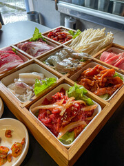 Box of fresh ingredients for Korean BBQ at a restaurant, featuring beef, pork, mushrooms, shrimp, and squid ready to grill at the table. A vibrant culinary experience awaits!