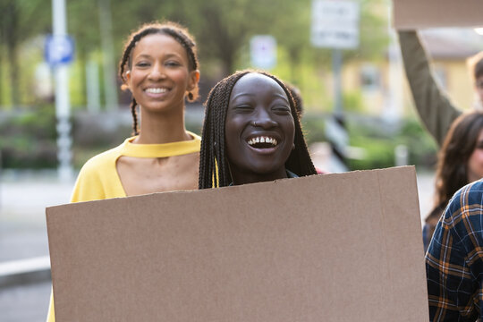 Diverse young women with blank protest sign: African activists smiling at social demonstration