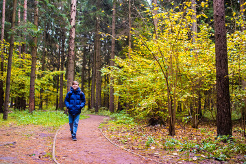 teenage boy in blue jacket walking in autumn forest or park