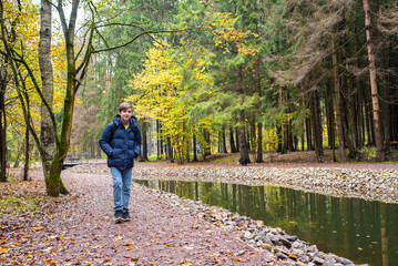 Fototapeta premium A 12 year old boy in a blue jacket walks along a cascade of ponds in Borovsky Park in autumn.