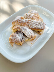 Delicious chocolate croissant on a sunlit terrace table at a cozy snack bar, perfect for breakfast or a sweet treat. Ideal for food photography and café lifestyle themes.