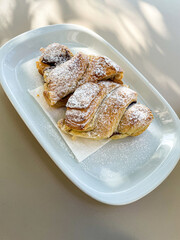 Delicious chocolate croissant on a sunlit terrace table at a cozy snack bar, perfect for breakfast or a sweet treat. Ideal for food photography and café lifestyle themes.