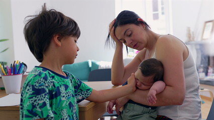 Mother cradles a sleeping baby while engaging in a tender conversation with her older child at the table, capturing a warm and intimate family moment filled with love and connection