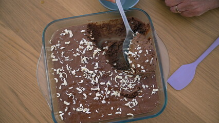 Overhead view of a homemade chocolate dessert being served, topped with white chocolate shavings, capturing the rich and creamy texture in a relaxed home dining environment