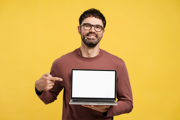 Handsome hispanic man wearing eyeglasses, holding laptop, pointing finger on white blank screen