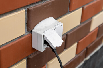 Outdoor electrical outlet on the wall of brick house. Snow and ice on the outdoor outlet
