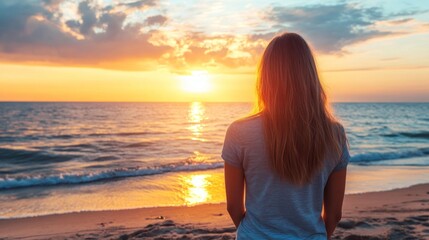 Fototapeta premium A woman stands on a sandy beach, gazing at the sunset over the ocean.