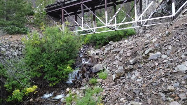 Historic Morley railroad bridge near St. Elmo, Colorado. No longer used for trains, it remains intact for historical reasons. Flight travels along a stream, up and over the bridge to reveal forest.