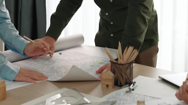 Smart architect and safety engineer discussion about building blueprint on table with architectural document, measurement tools and wooden block scatter around at modern office. Closeup. Delineation.