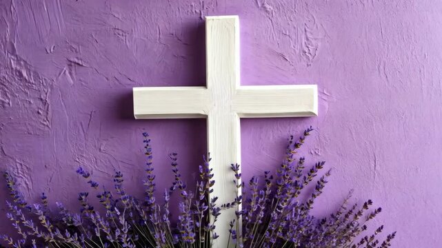 A white cross rests on a purple wall, surrounded by lavender flowers