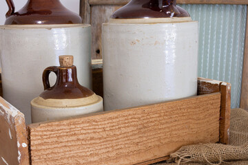 An image of three vintage ceramic whiskey jugs in an old wooden crate and packed with burlap. 