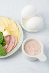 Light breakfast, boiled eggs, plate with cheese, ham and spinach.