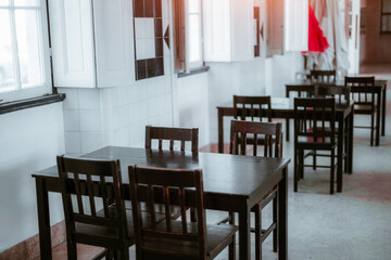 An empty, minimalist indoor dining space with dark wooden tables and chairs in Leiria. Sunlight gently illuminates the room through windows, creating a calm, serene atmosphere; shallow depth of field