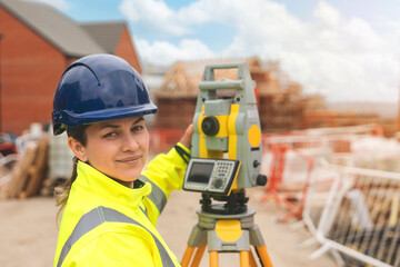 Confident female surveyor in a hard hat uses a total station at a construction site on a sunny day