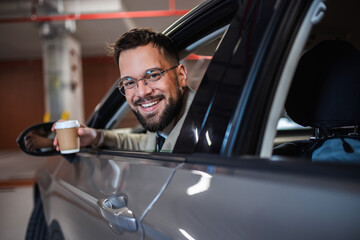 Portrait of young businessman sticking his head out of the window smiling and holding coffee.