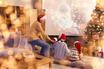 Happy family in Santa hats watching Christmas movie on projector screen at home