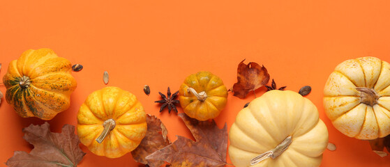 Fresh pumpkins with star anise, seeds and autumn leaves on orange background