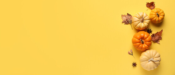 Fresh pumpkins with star anise and autumn leaves on yellow background