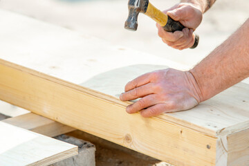 Joiner carpenter assembling formwork shutter. Crafting a wooden structure with precise hammer strikes at a sunny outdoor workshop in the afternoon