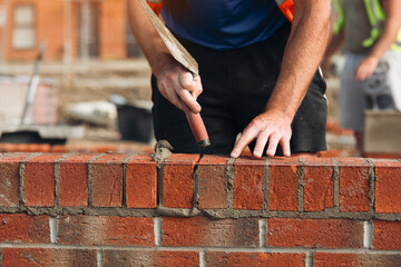 Skilled bricklayer meticulously laying bricks on a construction site under bright sunlight in a...
