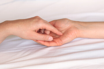 Same-sex relationships, lesbians. Two female hands touching each other against white sheets. Two female hands in bed close-up. LGBTQ, love concept.