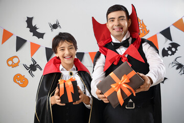 Little boy and his father dressed for Halloween as vampires with gifts on light background
