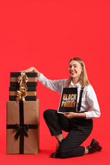 Young woman with card and gifts on red background. Black Friday sale