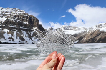 Tourist is holding a piece of ice with a frozen lake and snow-capped mountains in the background
