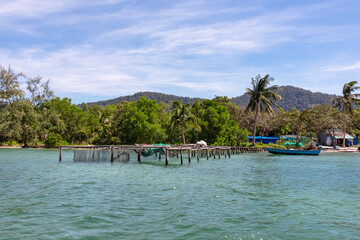 Aquaculture on floating platform surrounded by fishing nets and boats in fishermen village Rach Vem on Phu Quoc island, Vietnam, South East Asia. Local fish farming in turquoise water. Coastal scene