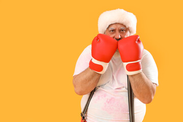 Sporty Santa Claus with boxing gloves on yellow background