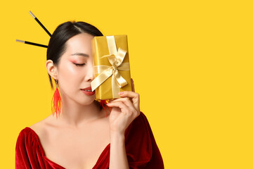 Beautiful young Asian woman with gift box on yellow background. Chinese New Year celebration