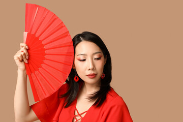 Beautiful young Asian woman with fan on brown background. Chinese New Year celebration