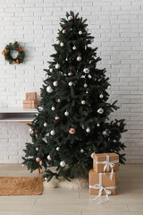 Beautiful Christmas tree with desk and gift boxes near white brick wall