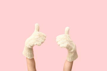 Hands in warm mittens showing thumbs-up on pink background