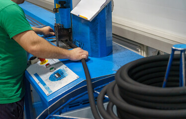 A worker cuts a long rubber hose into smaller pieces using a machine. Workplace with a machine...