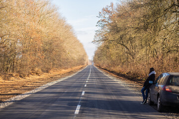 A beautiful girl stands on the road near the car around the autumn landscape