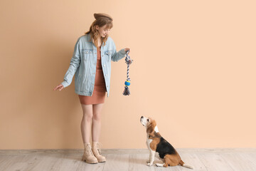 Young woman in casual attire playing with cute beagle dog on beige background