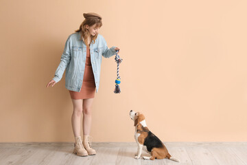 Young woman in casual attire playing with cute beagle dog on beige background